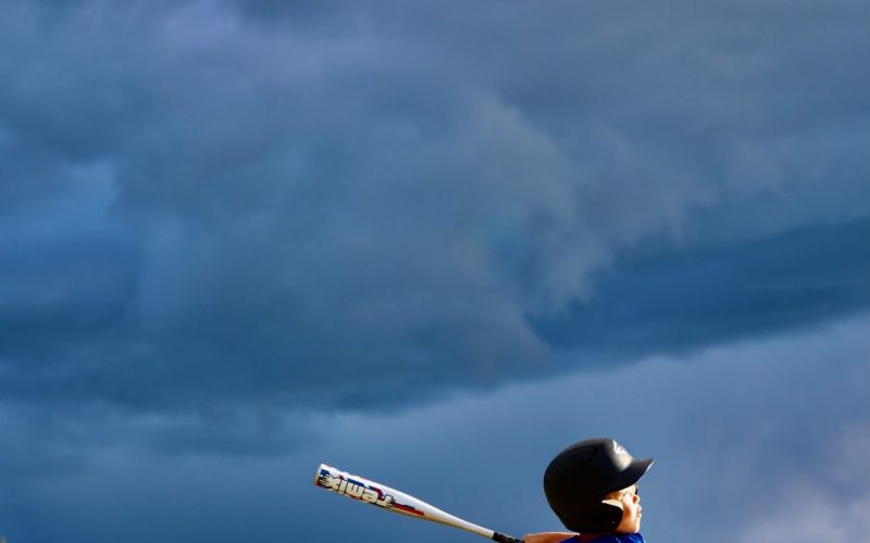 Young batter swinging under a dramatic storm sky